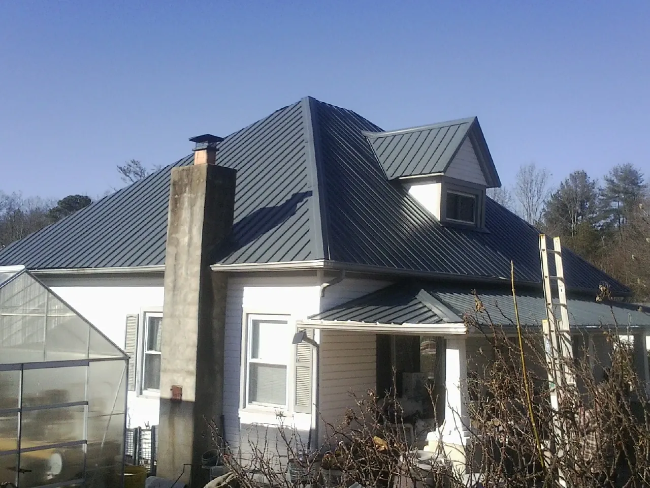Dark blue standing seam metal roof on a white farmhouse with dormer — Slate & Tile Roof Repair by Roofing Brothers in Mayetta
