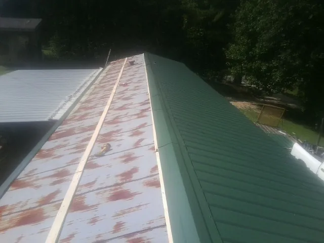 Old rusted panels beside newly installed green metal roofing — Wind Damage Roof Repair by Roofing Brothers in Mayetta