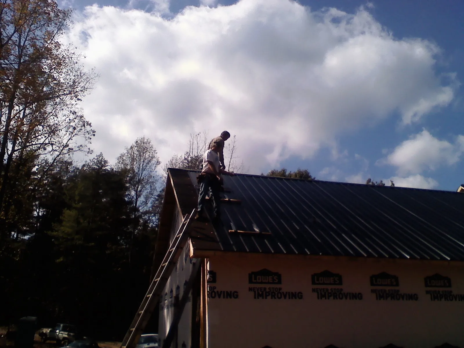 Roofer fastening dark metal panels high against a cloudy sky, from a Roof Inspection job in Mayetta